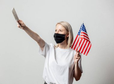 Amerika bayrağı ve beyaz arka planda parası olan maskeli sarışın kız.