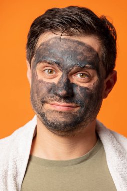 Yüzünde kozmetik maske ve turuncu arka planda havlu olan komik bir adam.