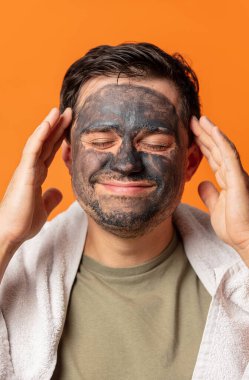 Yüzünde kozmetik maske ve turuncu arka planda havlu olan komik bir adam.