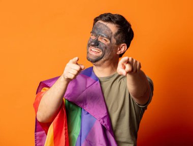 Yüzünde kozmetik maske olan ve elinde LGBT bayrağı olan komik bir adam. 