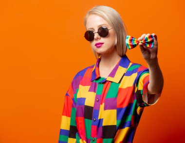 Turuncu arka planda LGBT papyonlu 90 'ların kıyafetleri içindeki tarz sarışın.