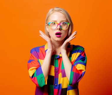 90 'ların kıyafetleri ve turuncu arka planda gökkuşağı gözlüklü tarz sarışın.