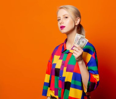 90 'ların kıyafetleri içinde, turuncu arka planda dolarları olan tarz sarışın.