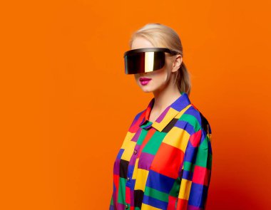 90 'lı yılların moda sarışını turuncu arka planda VR gözlükler.