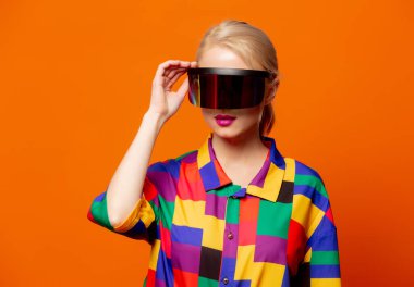 90 'lı yılların moda sarışını turuncu arka planda VR gözlükler.