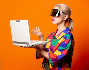 90 'ların kıyafetleri içinde, turuncu arka planda defter ve VR gözlükleri olan tarz sarışın.