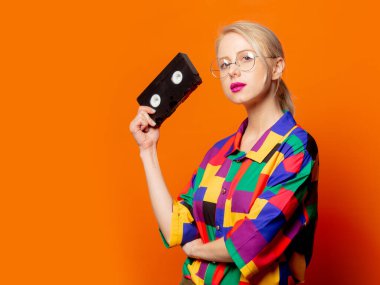 90 'ların tişörtlü, gözlüklü, turuncu arka planda VHS tipi sarışın.