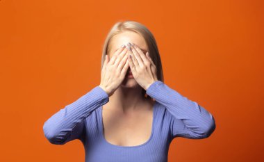 Mavi bluzlu, parlak turuncu arka planda baş ağrısı olan hoş bir sarışın. 