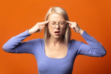 Mavi bluzlu, parlak turuncu arka planda baş ağrısı olan hoş bir sarışın.