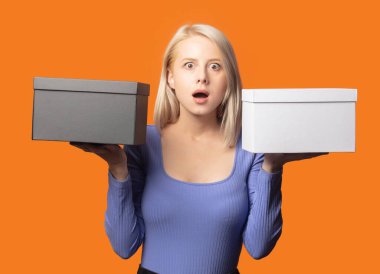 Mavi bluzlu şirin sarışın, turuncu renkli arka planda iki hediye kutusu var.