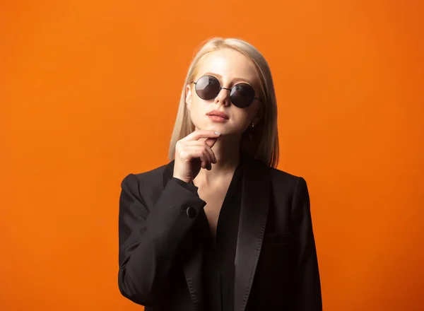 Stylische Blondine Schwarzem Blazer Und Sonnenbrille Vor Üppigem Orangefarbenem Hintergrund — Stockfoto
