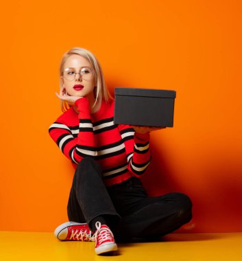 Gfit kutulu stil hippi kız turuncu arka planda bir yerde oturuyor.