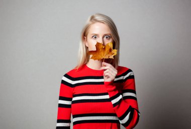 Gri arka planda akçaağaç yaprağı olan kırmızı süveterli stil kızı.