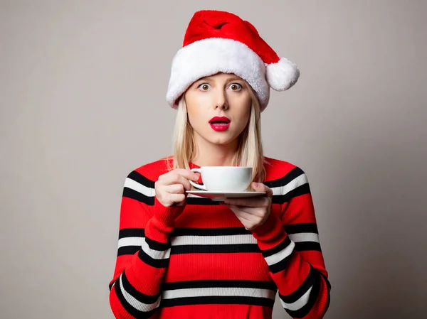 笑顔女の子でクリスマスの帽子とともにコーヒーのカップの灰色の背景 — ストック写真