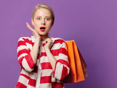 Kırmızı ceketli güzel sarışın, arkaplanda alışveriş torbaları var.