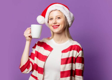 Kırmızı ceketli güzel sarışın ve mor arka planda Noel şapkalı. 