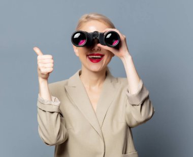 Gri arka planda dürbünü olan ceketli şık bir sarışın.