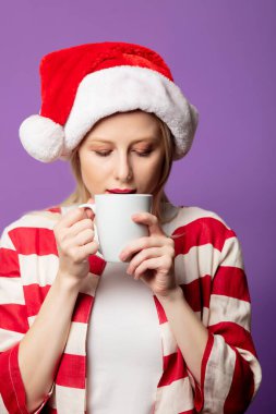 Kırmızı ceketli güzel sarışın ve mor arka planda Noel şapkalı. 