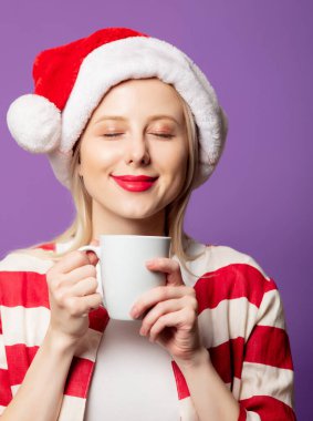 Kırmızı ceketli güzel sarışın ve mor arka planda Noel şapkalı. 