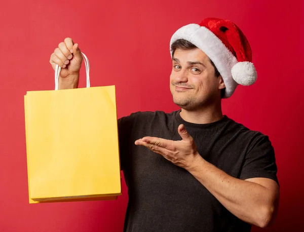 Mann Mit Weihnachtsmütze Und Schwarzem Shirt Mit Einkaufstaschen Auf Rotem — Stockfoto