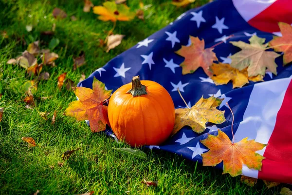 Little pumpkin and maple leaves with USA flag on green grass in a garden