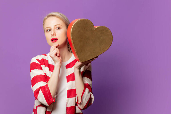 Beautiful blonde in red jacket with heart shape gift box on purple background