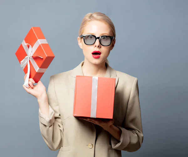 Stil Blond Jacka Och Glasögon Håller Presentförpackning Grå Bakgrund — Stockfoto