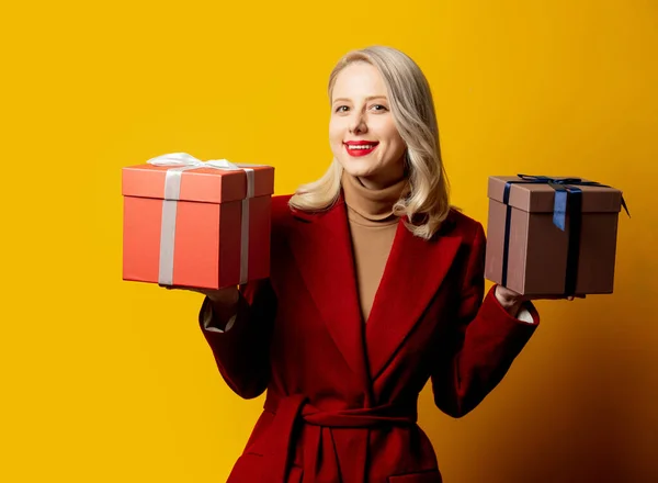 Блондинка Красном Пальто Подарочными Коробками Желтом Фоне — стоковое фото