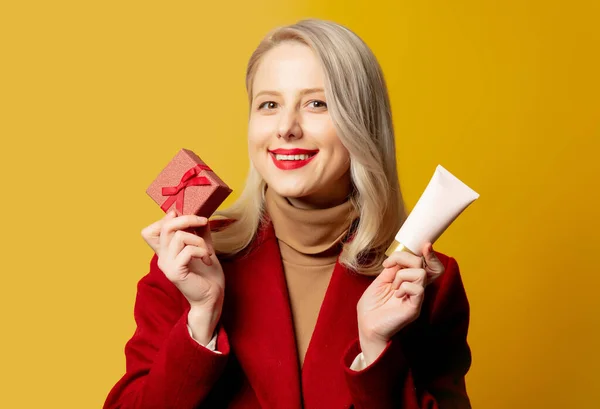 Beautiful Woman Red Coat Gift Box Cream Tube Yellow Background — Stock Photo, Image