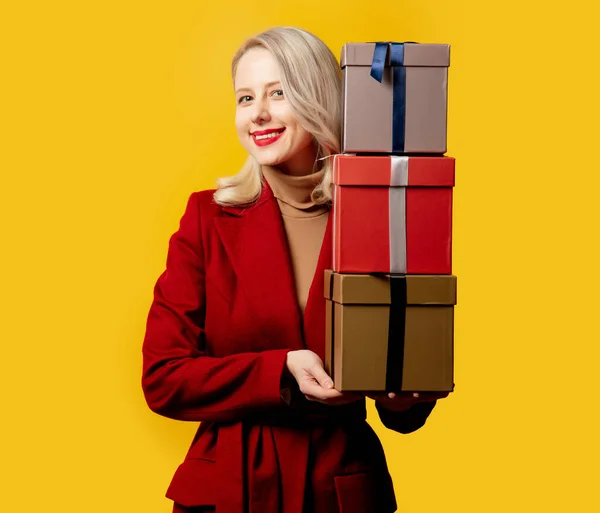 Blonde Smiling Woman Red Coat Gift Boxes Yellow Background — Stock Photo, Image