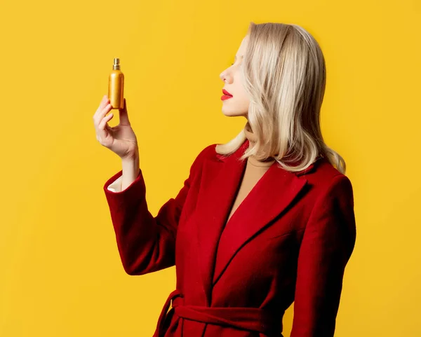 黄色の背景に香水付きの赤いコートの女性 — ストック写真