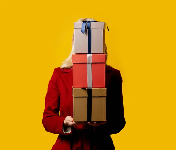 Sarı Arka Planda Hediye Kutuları Olan Kırmızı Ceketli Sarışın Kadın — Stok fotoğraf