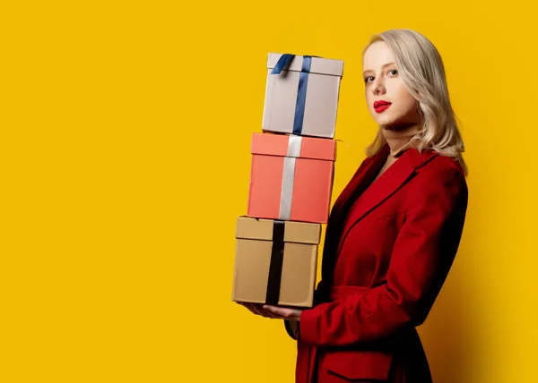 Blondýny Žena Červeném Kabátu Dárkovými Krabicemi Žlutém Pozadí — Stock fotografie