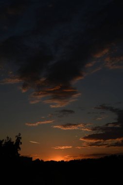 Kızıl gökyüzü, ağaçlar ve bulutlarla güzel renkli bir gün batımı.