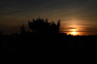 Kızıl gökyüzü, ağaçlar ve bulutlarla güzel renkli bir gün batımı.