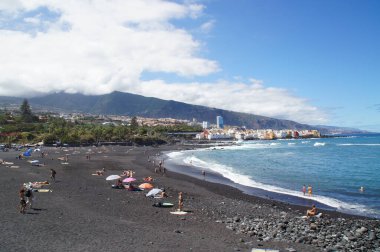 İspanyol Kanarya Adası 'ndaki güzel Playa Jardin plajı siyah volkanik kum, mavi okyanus suyu ve yeşil palmiye ağaçları ile Tenerife