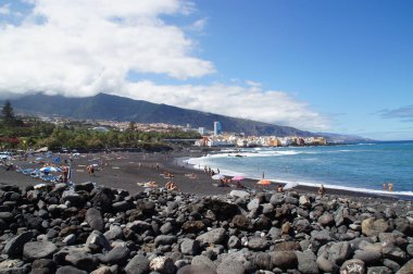 İspanyol Kanarya Adası 'ndaki güzel Playa Jardin plajı siyah volkanik kum, mavi okyanus suyu ve yeşil palmiye ağaçları ile Tenerife