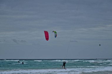 Koyu bulutlu dalgalar ve kıyıda yüzen paraşütlü sörf takımıyla okyanusla güzel bir yaz manzarası.