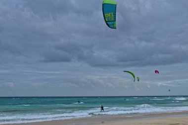 Koyu bulutlu dalgalar ve kıyıda yüzen paraşütlü sörf takımıyla okyanusla güzel bir yaz manzarası.