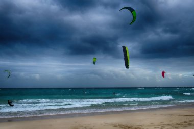 Koyu bulutlu dalgalar ve kıyıda yüzen paraşütlü sörf takımıyla okyanusla güzel bir yaz manzarası.