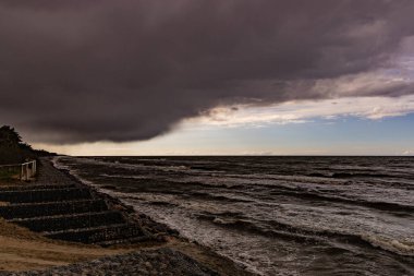 Su dalgaları, plaj ve baharda yaklaşan karanlık tehditkar fırtına bulutlarıyla güzel bir deniz manzarası.