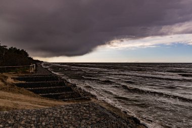 Su dalgaları, plaj ve baharda yaklaşan karanlık tehditkar fırtına bulutlarıyla güzel bir deniz manzarası.
