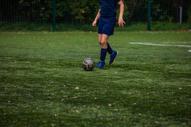 Yapay yeşil çimlerde futbol oynayan bir çocuğun bacaklarına yakın plan.