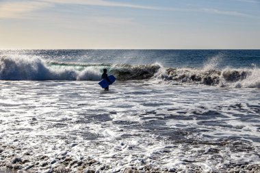 Sıcak ve güneşli bir yaz gününde dalgalı okyanusların arka planında bir sörfçünün silueti,