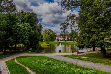 Serene Park ayarı, merkezi bir çeşmeyle çevrili küçük bir göleti çevreleyen yemyeşil yeşilliklere sahiptir.