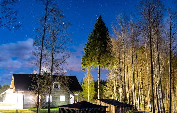 Night landscape - a lighting house in the forest against the sky with stars