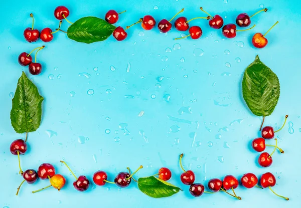 Marco sobre fondo turquesa con cerezas y hojas verdes — Foto de Stock