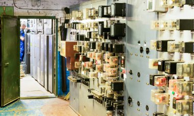 İnsanlar bir elektrik santralindeki röle odasında çalışıyorlar.