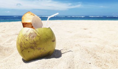 Taze hindistan cevizi, kumsalın arka planında içilmeye hazır pipetle yatıyor. Tropik tatil seyahati konsepti. Uzayı kopyala Beyaz kumlu hedef