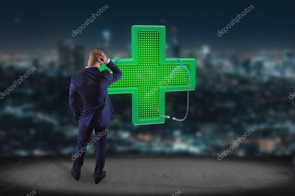 Businessman in front of a wall with green pharmacy cross and stethoscope - 3d rendering